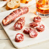 Image of Marinated Olive Salami. 1 link, 3 oz. an original pork salami made with preserved lemon, roasted garlic, and a trio of olives- oil-cured, Castelvetrano, and Manzanilla